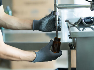 A worker wearing grey textured safety gloves uses a metallic filling machine to precisely fill a...