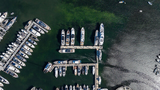 A direct overhead aerial photo above a sunny dock filled with moored leisure craft and yachts are seen below