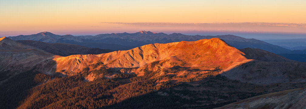 This scenic Colorado sunrise panorama features Wander Ridge with the Continental Divide Trail cutting across its slope near Cottonwood Pass, glowing in soft orange light.