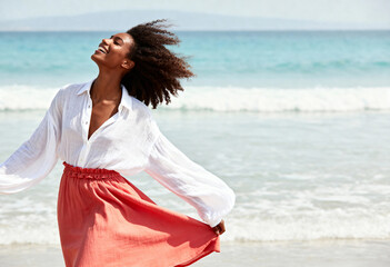 Happy black woman smiling on the beach with wind in her hair. Young adult enjoying a summer vacation by the ocean. Freedom and carefree lifestyle concept with copy space