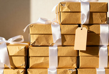 Stack of wrapped gift boxes with white ribbons and blank tag. Brown kraft paper presents with copy space. Holiday or birthday celebration background