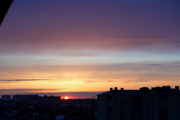 The image shows a calm pond with rocks in the foreground. Mountains are visible in the distance. The sky is colored in shades of sunset or dawn, with clouds.