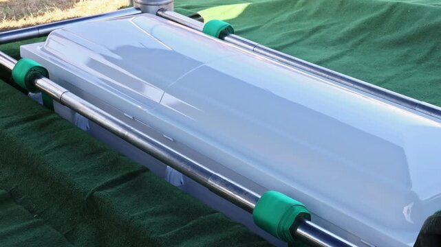 Casket rests on green cloth with metal rods, ready for burial at cemetery during funeral service