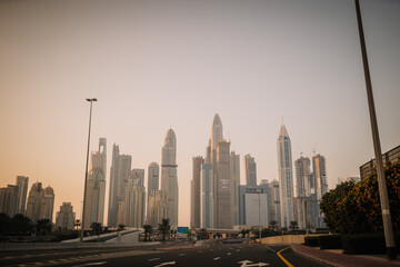 Obraz premium Modern skyscrapers in a city skyline during sunset with a clear sky and road in the foreground, showcasing architectural diversity and urban development