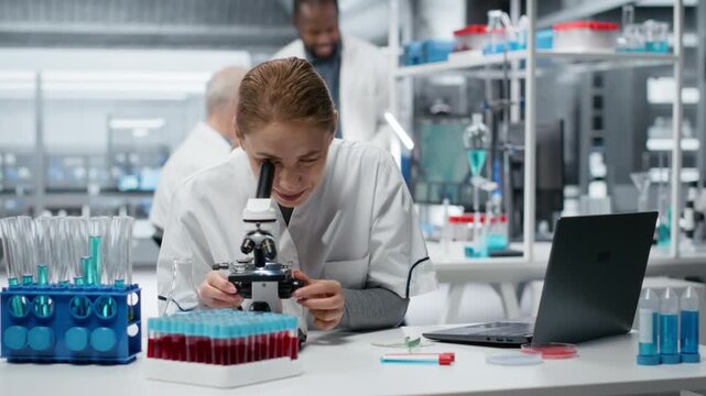 Portrait of smiling scientist examining pathology slides under microscope in research center. Happy woman driving medical innovation through dedicated cellular analysis work, camera B