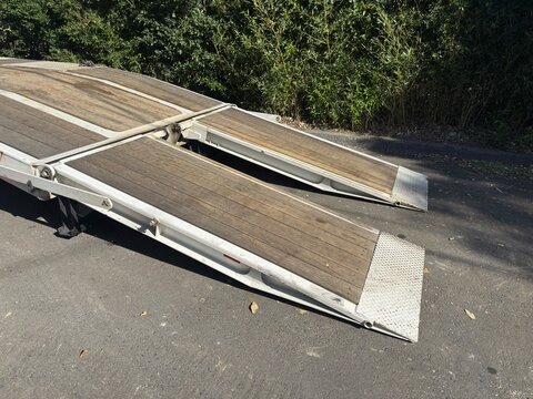 Wooden Trailer Ramp: Heavy-duty ramp on a flatbed trailer used for loading industrial construction equipment.