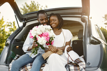 Young happy couple in a park sitting in car trunk