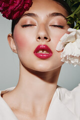 Close-up portrait of a woman with glossy red lips and soft rosy makeup. She poses with closed eyes...
