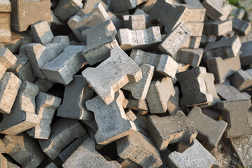 Heap of H-shaped interlocking concrete paving stones. Pile of grey pavers ready for installation at a construction site. Textured industrial background of building materials.