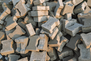 Heap of H-shaped interlocking concrete paving stones. Pile of grey pavers ready for installation at a construction site. Textured industrial background of building materials.