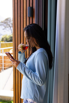 Smartphone resting on doorway frame while glass cup steaming on balcony near wooden slats