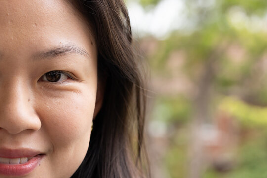 Adult Asian female smiling while looking at camera outdoors in park with stud earring, copy space
