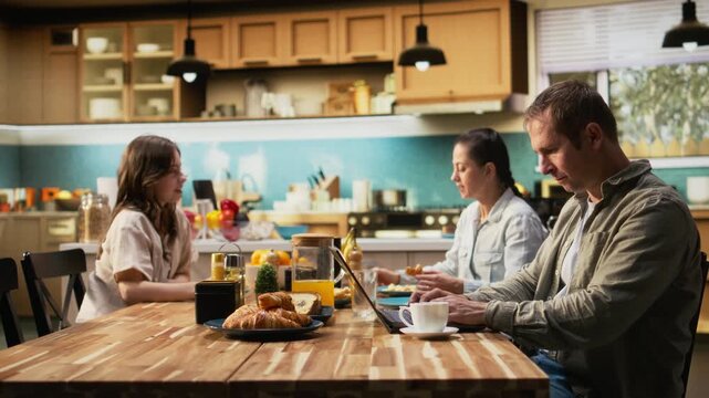 Busy father ignoring his daughter at breakfast table and focusing on work, typing information on laptop and looking preoccupied. Distant working dad with a career and pre-teen girl. Camera A.