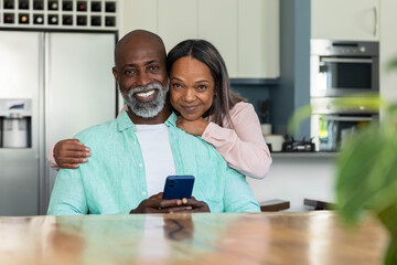 Diverse couple smiling and holding blue smartphone at wooden island, wearing mint green shirt