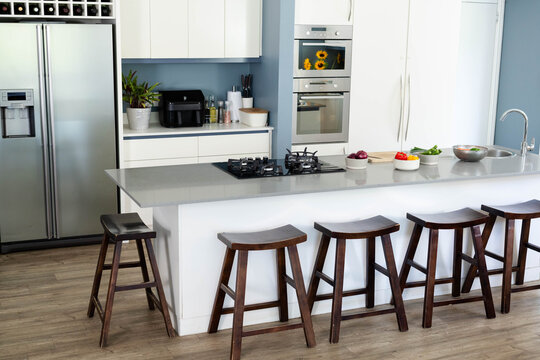 Kitchen island is anchoring modern kitchen with gray stone countertop, six stools, gas cooktop