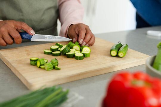 Zucchini being sliced on wooden cutting board with blue-handled chef knife on gray countertop