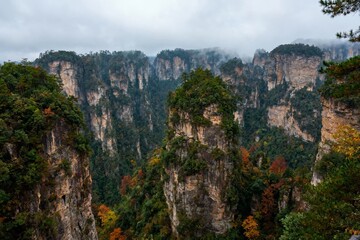Fototapeta premium Majestic forest-covered rock formations rise dramatically in a misty mountain landscape