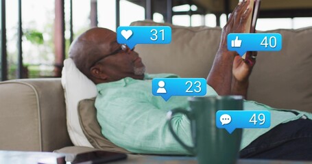 Reclining man wearing green shirt and glasses holding phone at home on sofa, with social alerts