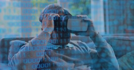 Adjusting senior man wearing knit sweater holding VR headset on sofa with cushions, binary overlay