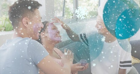Applying facial cream, three friends leaning on sofa at home, holding small jar, towel-wrapped head