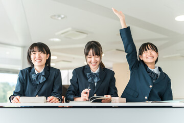 Active elementary school students, junior high school students, high school students, and female high school students (friends, classmates) in uniforms raising their hands during class in a school cla © buritora