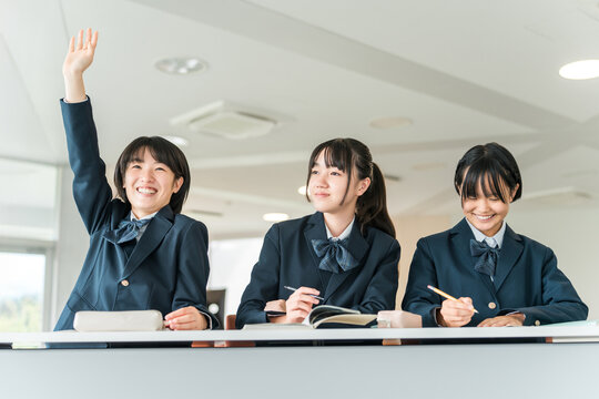 Active elementary school students, junior high school students, high school students, and female high school students (friends, classmates) in uniforms raising their hands during class in a school cla