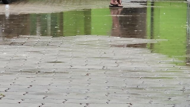 Person walking past puddles on wet pavement, rainy day footage. Bare legs stepping on soaked brick walkway, reflection water clip. Pedestrian crossing flooded sidewalk tiles, urban weather scene. 