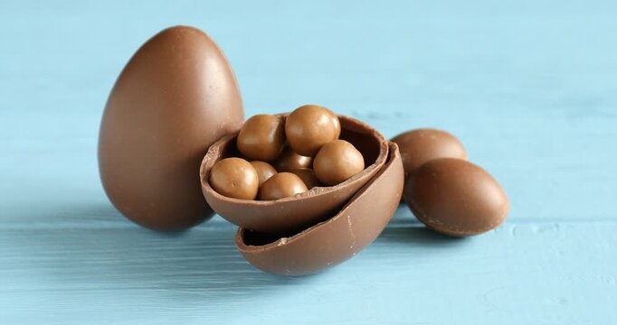 Candies falling into chocolate Easter egg on light blue wooden table, closeup