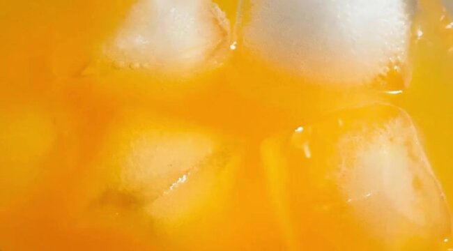 Extreme macro close-up of orange juice with ice cubes, showing bright citrus color, glossy liquid texture, cold condensation, refreshing clarity with a clean, food-texture focus, orange juice video.