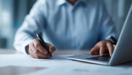 Business person writing notes on paper, working with a laptop. Close up of hands on office desk. Productivity and planning