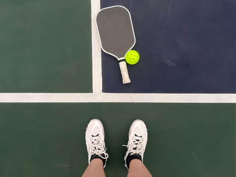 Top view of a woman shoes, Pickleball paddle and ball in a green and blue court