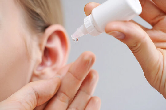 Person applying ear drops from a white plastic bottle into an ear medicine liquid