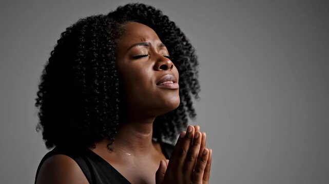 Woman with eyes closed and hands clasped in prayer, looking upwards with hope