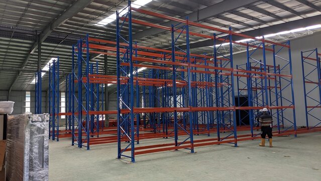 Empty Industrial Warehouse Interior with Blue and Orange Metal Pallet Racking Systems and High Ceiling Skylights
