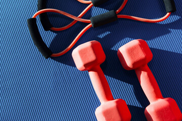 Top view of mat placed on floor with rubber expander and two dumbbells in fitness club