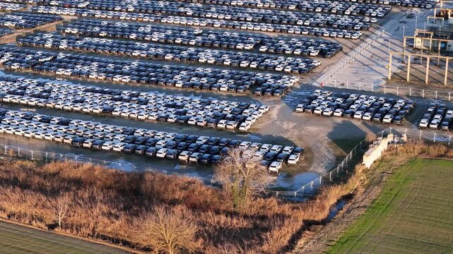 Overhead aerial view documents an automotive logistics yard with imported vehicles stored in dense, organized rows, illustrating industrial scale transport infrastructure and supply chain operations