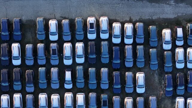 Top down drone reveal suv and cars parked in spaced parallel rows within a parking lot, highlighting organized vehicle storage for commercial dealers supply chain