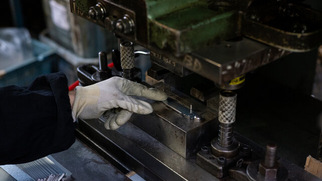 Metal press machine operation with worker adjusting parts during production in small factory