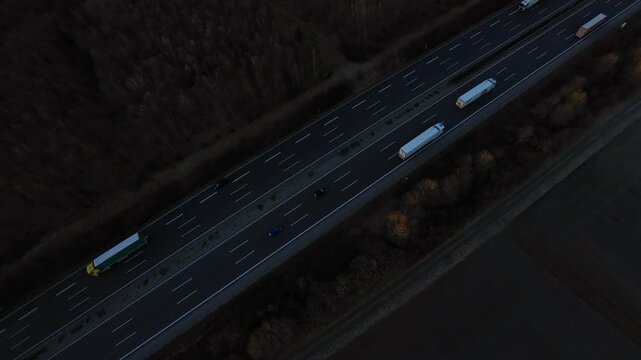 Transport trucks driving on road at dawn with surrounding agricultural landscape Dark highway with moving trucks in early morning light cutting through empty countryside