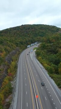 Vertical Screen, USA Aerial Curved Highway Through Forest Overcast Sky, Light Traffic Winding Along Hillside With Guardrail And Fall Foliage, Lone Commuter Navigating Bend Captured By Drone