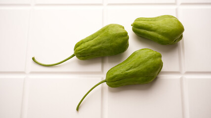 A pile of green chayote squash on white table