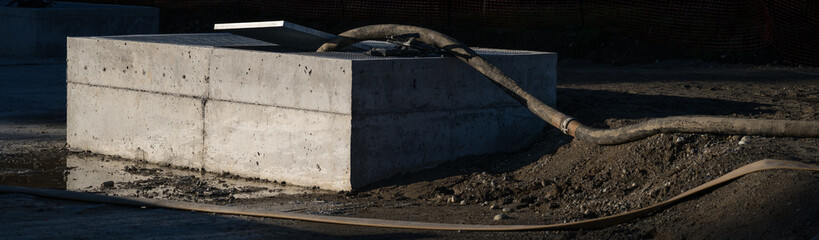 Obraz premium Underground stormwater tank with camlock industrial heavy duty dewatering hose for pumping out rainwater running across stie to access point, new construction job site 