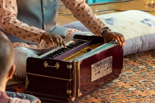 Close-up of musicians hands operating keys and bellows of traditional Indian instrument harmonium. Selective focus