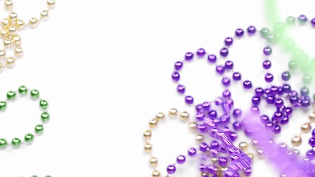 Pile of Mardi Gras beads in yellow or gold green and purple. Slow motion throwing of Mardi Gra bead necklaces covering white background. Celebrating Mardi Gras, aka Fat Tuesday.