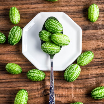 Cucamelons (Melothria scabra) on and around a decorative metal spoon against a white octagonal plate