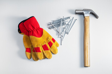 DIY and home improvement concept. Top view of hammer, gloves and metal nails on grey background.