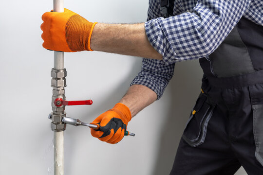 A plumber in uniform is working on a pipe that is dripping water. Fix water plumbing leaks in outdoor.