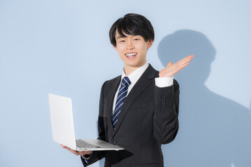 水色背景でパソコンを持つタイピングするスーツの若い大学生のような男性　新卒や就職のビジネスイメージ　就活の採用イメージ　オススメのポイント