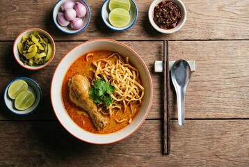 Northern Thai khao soi soup with chicken leg, curry broth, and crispy noodles, served with various condiments on a wooden table.