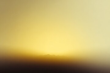 Atmospheric golden hour image depicting hazy mountain range silhouetted against a gradient sky